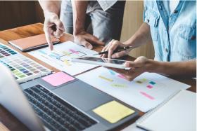 two individuals reviewing documents and a laptop, working on a project