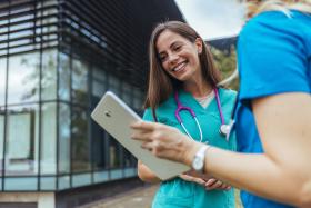 female nurse talking to another glancing at a tablet